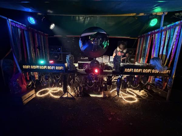 This vibrant photo captures a DJ setup illuminated by an array of colorful neon lights and spotlights at Haarweg, Vuren